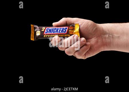 Hand hält eine Schokoladenriegel in Nahaufnahme. Ein Mann bietet eine Schokoriegel von Snickers mit schwarzem Hintergrund an Stockfoto