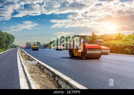 Die Baustelle legt neue Asphaltbelag, Straßenbauarbeiter und Straßenbaumaschinen Szene. Autobahn Baustelle Szene. Stockfoto