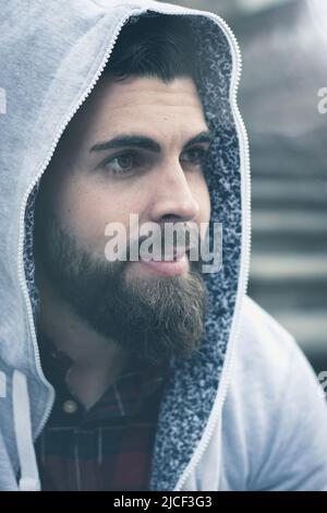 Nahaufnahme eines jungen Mannes mit Vollbart und grauem Hoodie auf dem Kopf. Hip-Hop, Rapper-Style. Hipster männlich Modell Porträt. Lichteffekt Stockfoto