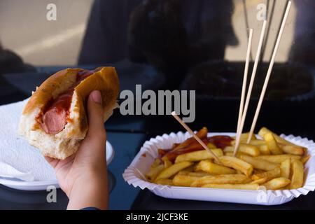 Hand halten Hot Dog von pommes frites Platte. Fast Food, ungesunde Ernährung, Ketchup-Sauce, leckere Konzepte Stockfoto