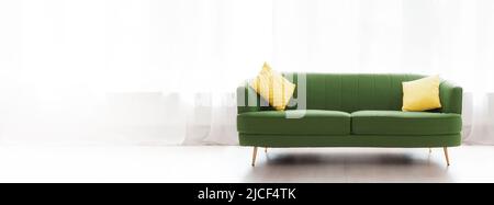 Renovierung der Wohnung. Gemütliches grünes Sofa mit gelben Kissen auf Fensterhintergründen. Banner mit Kopierbereich. Das Konzept des Einkaufs und Mietens von hous Stockfoto