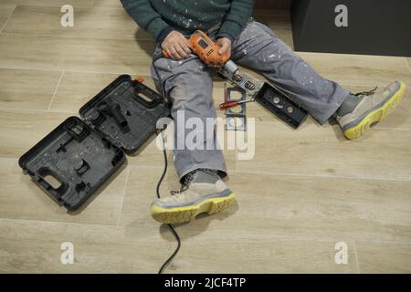 Nicht erkennbarer Elektriker, der eine Bohrmaschine hält, um eine Eckbuchse zu installieren. Stockfoto