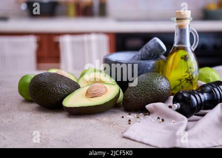 Frische Avocado in zwei Hälften geschnitten und Marmormörtel auf grauem Betontisch Stockfoto