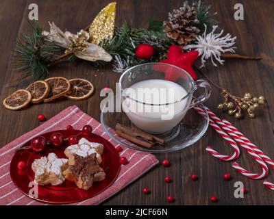 Weihnachtsdekoration mit Zuckerstöcken, sternförmigen Keksen, getrockneten Orangenscheiben und einer Glasschale mit Milch Stockfoto