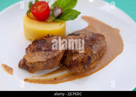 Fleischbällchen mit Kartoffelpüree auf einem weißen Teller. Fleisch in saurer Rahmsoße. Tomaten und Basilikum. Essen im Restaurant. Mittagspause. Medaillons. Stockfoto