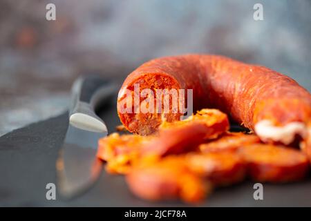 Spanischer Chorizo wurde mit einem Messer auf einem Schieferschneidebrett geschnitten. Stockfoto