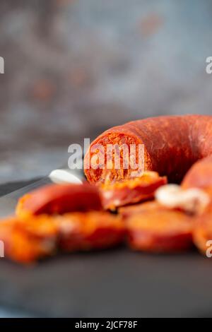Spanischer Chorizo wurde mit einem Messer auf einem Schieferschneidebrett geschnitten. Stockfoto