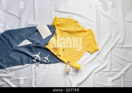 Ein gelbes Crop-Shirt gepaart mit einer hellen Vintage-Jeans. Kommt mit drei kleinen Flugzeugen, einem Stück Papierpostkarte, und die Küken Puppe auf weiß b Stockfoto