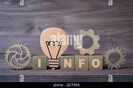 WORTINFO aus hölzernen Spielzeugblöcken mit Zahnrädern und einer hölzernen Glühbirnenform auf einem hölzernen Hintergrund. Kreatives Konzept zur Ideenentwicklung. Stockfoto