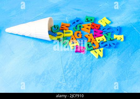 Geschmolzenes Eis-Symbol aus einem Waffelkegel und einem Haufen von bunten Holzbuchstaben auf einem blauen texturierten Hintergrund mit Kopierraum angeordnet. Cre Stockfoto