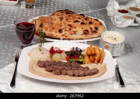 Shish Kebab wird aus Lamm hergestellt. Auf dem Esstisch stehen Shish Kebab, Pita-Brot und Fruchtsaft. Stockfoto