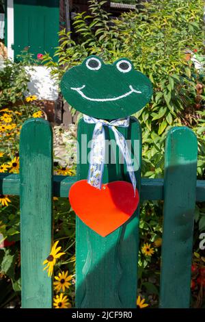 Fröhlicher grüner Frosch mit rotem Herzen auf einem Gartenzaun Stockfoto