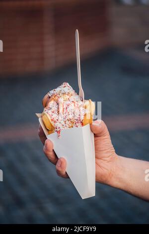 Hand hält eine Blasenwaffel mit Eis, Erdbeersoße und Kokosflocken Stockfoto