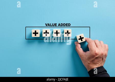 Männliche Hand legt den Holzwürfel mit Plus-Symbol mit dem Wort Mehrwert. Gewinn, Nutzenwachstum und Entwicklung von Geschäftskonzepten. Stockfoto