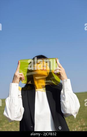 Modisch gekleidete Frau mit gelber Folie vor dem Gesicht Stockfoto