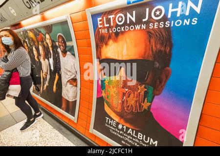 England, London, U-Bahnhofsplattform mit Elton John Album Werbeplakat und weiblicher Passagierin mit chirurgischer Maske Stockfoto