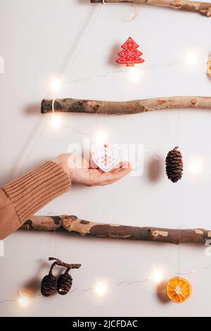 Frauenhänden schmücken Weihnachtsbaum aus trockenen Stäben, trocken orange, Zapfen auf weißem Hintergrund. Zero Waste Weihnachten, Neujahr, umweltfreundliche Konz Stockfoto