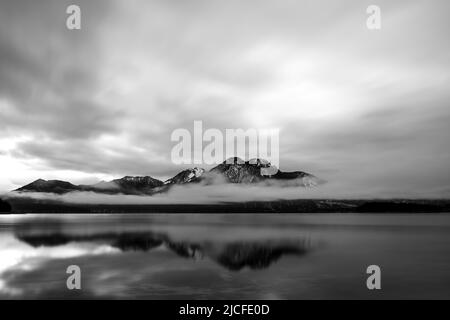 Dichte Wolken und Nebel am Walchensee, Herzogstand und Heimgarten spiegeln sich im klaren Wasser des Alpen-See. Stockfoto