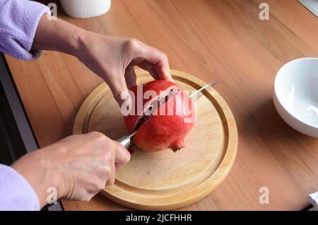 Schneiden und Öffnen einer roten Granatapfelfrucht (Punica granatum) mit einem Messer auf einem Holzbrett Stockfoto