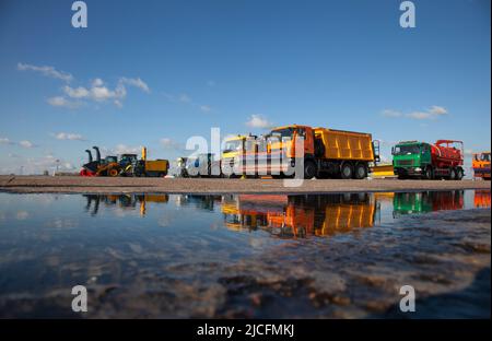 Bunte Autos. Schneefräse. Große Schneeräummaschinen am Flughafen. Straßenausstattung. Grader, Muldenkipper, Traktor. Das neue Auto spiegelt sich in einer Pfütze wider. Reflexion. Im Freien Stockfoto