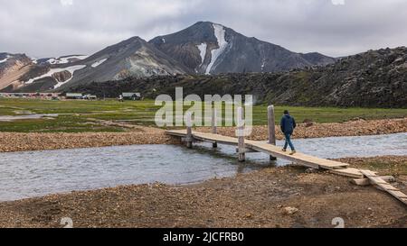 Der Laugavegur-Wanderweg ist die berühmteste mehrtägige Trekkingtour in Island. Landschaft aufgenommen aus dem Gebiet um Landmannalaugar, Ausgangspunkt des Fernwanderweges im Hochland Islands. Wanderer geht über die Brücke. Stockfoto