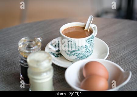 Kaffee mit gekochten Eiern, Sojasauce und weißem Pfeffer auf dem Tisch. Traditionelles orientalisch-chinesisches kopitiam-Frühstück. Stockfoto