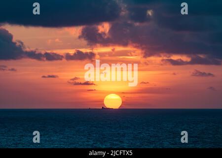 Ein Sonnenuntergang über dem Meer fällt mit einem vorbeifahrenden Containerschiff zusammen. Entnommen aus Crown Mines in Botallack, West Cornwall. Stockfoto