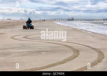 Mann mit Handicap fährt mit seinem Strandrollstuhl Serpentinenlinien am Strand Stockfoto
