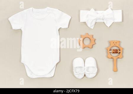 Modell mit weißem Babybody, Babyschühchen und Stirnband auf einem pastellbeigen Hintergrund im Öko-Stil. Baby hölzerne Beißringe und Rassel neben weißem rom Stockfoto