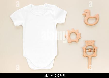 Babykleidung Mockup mit hölzernen Beißringe auf pastellbraunem Hintergrund im Öko-Stil. Handgemachte Holzspielzeug und Rasseln für Mockup mit weißem Babybody Stockfoto