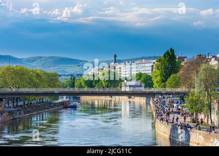 Wien, Donaukanal, Menschen sitzen auf Uferverstärkung, Blick auf die Müllverbrennungsanlage Spittelau, Entwurf Friedensreich Hundertwasser und Berg Kahlenberg im Jahr 01. Bezirk Altstadt, Wien, Österreich Stockfoto