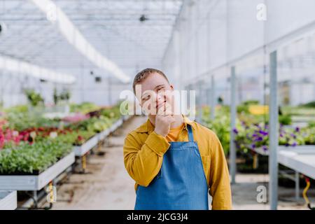 Junge Angestellte mit Down-Syndrom, die im Gartencenter arbeitet und die Kamera anschaut. Stockfoto