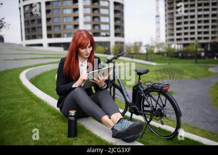Geschäftsfrau mit Fahrrad auf Treppen sitzend und mit Tablet. Pendeln und alternatives Transportkonzept Stockfoto
