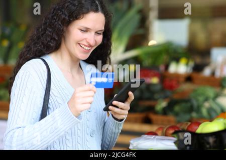 Glückliche Frau, die online mit Kreditkarte und Smartphone in einer Greengrocery kauft Stockfoto