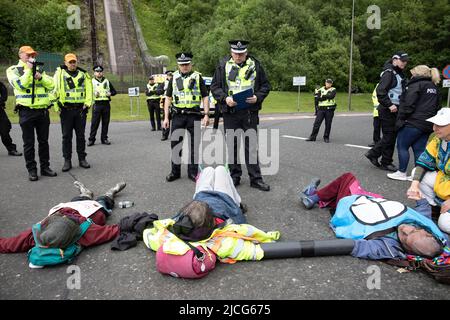 Coulport, Argyll, Schottland 13. Juni 2022 fünf ehemalige Greenham-Frauen und drei Mitglieder von Peace Pirates, einem Ableger von Trident Plowshares, führen eine Blockade im nuklearen Sprengkopflager von Coulport durch. Die ‘Greenham goss gefälschtes Blut auf sich selbst und inszenierten einen Einfall vor den Toren, der eine Seite des Eingangs in die Basis blockierte, während die Mitglieder von ‘Peace Pirates’ (pensionierter Lehrer Brian Quail, 84, mit einer Herztransplantation und durch einen kürzlichen Schlaganfall behindert, Willemien Hoogendorf aus Holland und Gillean Lawrence, eine Großmutter und Unterstützer von XR Peace) sperrten den Kreisverkehr weiter ein Stockfoto