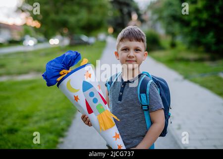 Kleiner Junge mit Schultasche am ersten Schultag, hält Schulkegel mit Geschenken Stockfoto