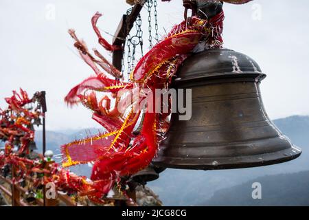 Eine Nahaufnahme von hängenden Glocken mit heiligen roten Tüchern mit schneebedeckten Bergen im Hintergrund, Kartik Swami Tempel, Rudraprayag Uttarakhand, in Stockfoto