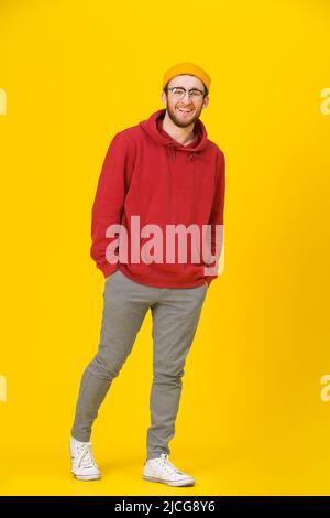 Ganzkörper-hübscher junger Mann in Freizeitkleidung, Brille mit Händen in Taschen, die vor gelbem Hintergrund die Kamera anschaut. Hipster Mode bärtig smart Mann casual Look. Stockfoto