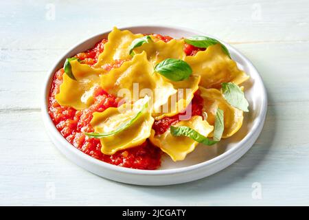 Ravioli mit Tomatensauce und frischen Basilikumblättern auf einem Teller, italienische Pasta-Gericht, auf einem rustikalen Holzhintergrund Stockfoto