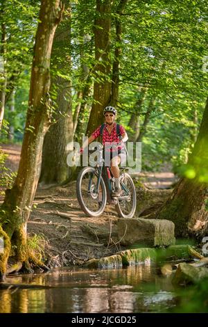 Nette aktive ältere Frau, die mit ihrem elektrischen Mountainbike im grünen Stadtwald von Stuttgart unterwegs ist Stockfoto