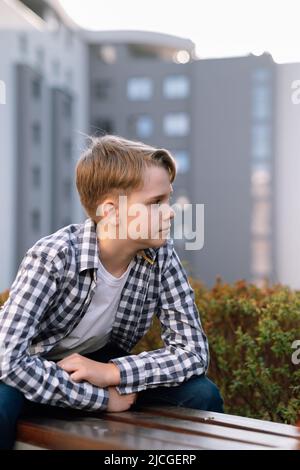 Ein stilvoller Teenager in legerer Kleidung entspannt sich im Freien auf einer Parkbank. Outdoor-Lifestyle. Stockfoto