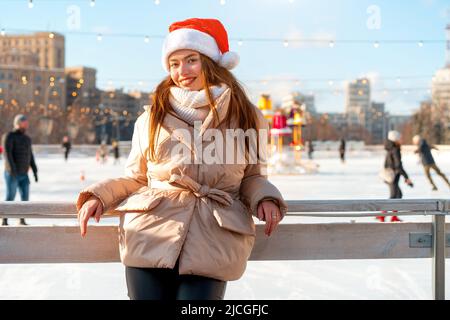 Outdoor-Porträt junge schöne modische Frau trägt Santa Hut, posiert Straße der europäischen Stadt. Winter Weihnachtsferien Konzept. Schlittschuhlaufen Stockfoto
