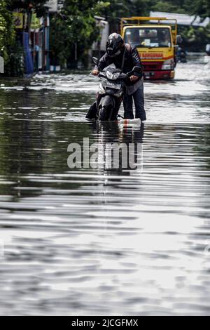 Sidoarjo, Indonesien. 13.. Juni 2022. Ein Mann geht mit seinem Motorrad nach heftigem Regen in Waru in Sidoarjo, Ost-Java, Indonesien, 13. Juni 2022 durch Hochwasser. Quelle: Kurniawan/Xinhua/Alamy Live News Stockfoto