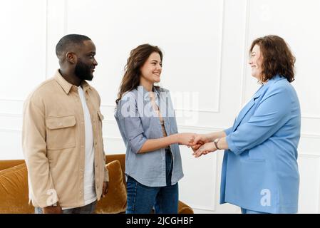 Eine weibliche Familienpsychologin schüttelt sich die Hände mit einer jungen Frau. Junges vielfältiges Paar Dank Psychologe für erfolgreiche Sitzung und gerettet Ehe. Stockfoto