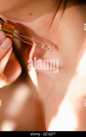 Eine Frau trägt Öl auf den Körper auf. Ein Tropfen ätherisches Öl tropft von einer Pipette auf das Schlüsselbein einer Frau. Serum für den Körper. Kosmetische Verfahren Stockfoto