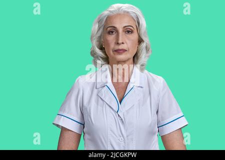 Porträt einer reifen Wissenschaftlerin oder eines Arztes, die die Kamera anschaut. Ältere Frau im weißen Mantel posiert auf grünem Hintergrund. Stockfoto