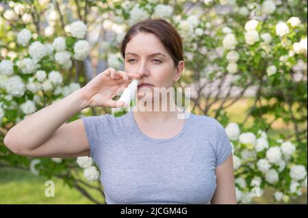 Kaukasische Frau verwendet ein Nasenspray, während sie im Park spazieren geht. Stockfoto