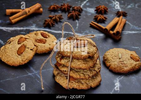 Haferflockenkekse mit Garn auf einem dunklen Tisch, umgeben von Zimtstangen und Sternanisgesteinen Stockfoto