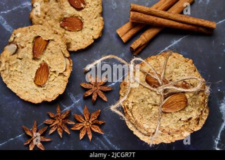 Haferflockenkekse mit Garn auf einem dunklen Tisch, umgeben von Zimtstangen und Sternanisgesteinen. Flach liegend Stockfoto