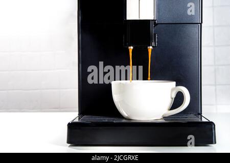 Frisch gebrühter Kaffee wird aus der Kaffeemaschine in eine weiße Keramikschale gegossen. Professionelle Kaffeemaschine für den Heimgebrauch Stockfoto